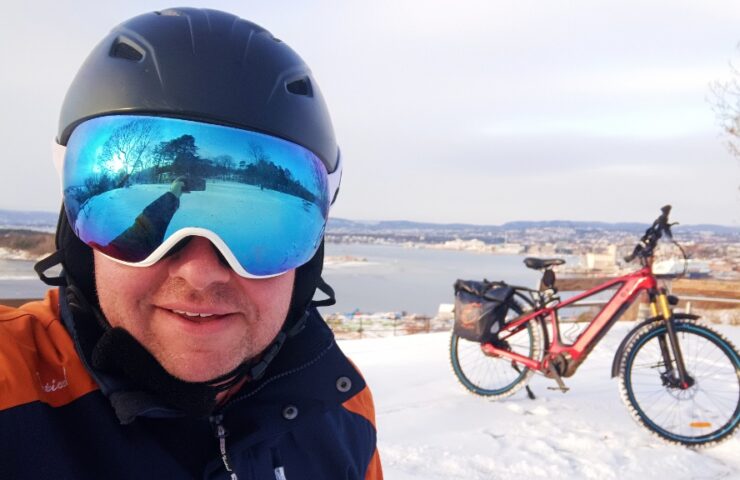 Gaute wearing a skiing helmet and googles in front of his bike, overseeing the Oslo fjord.