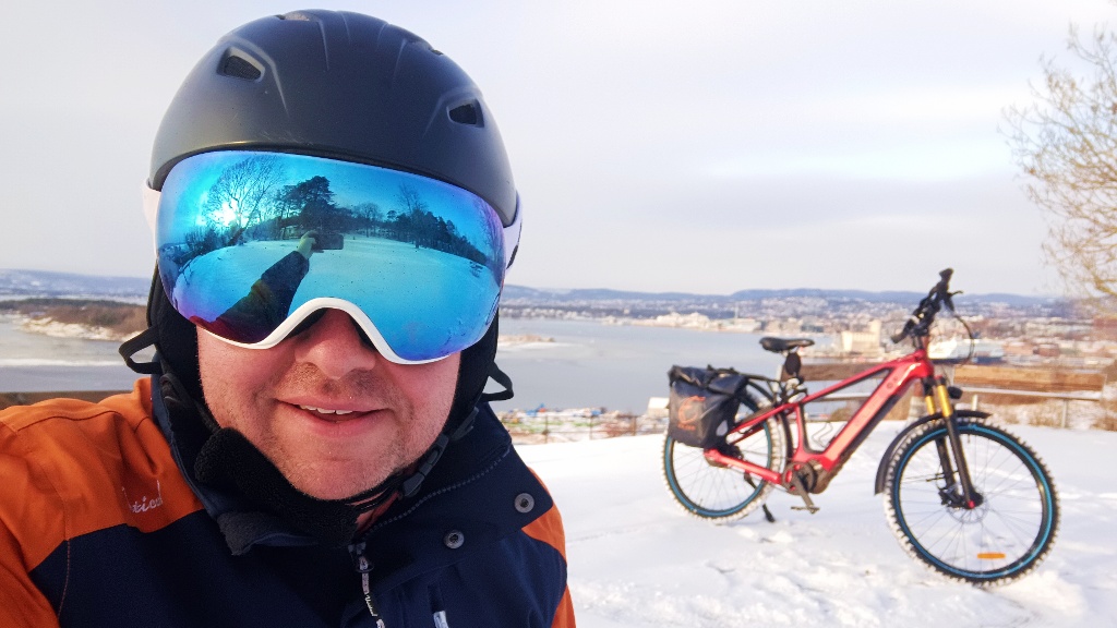 Gaute wearing a skiing helmet and googles in front of his bike, overseeing the Oslo fjord.
